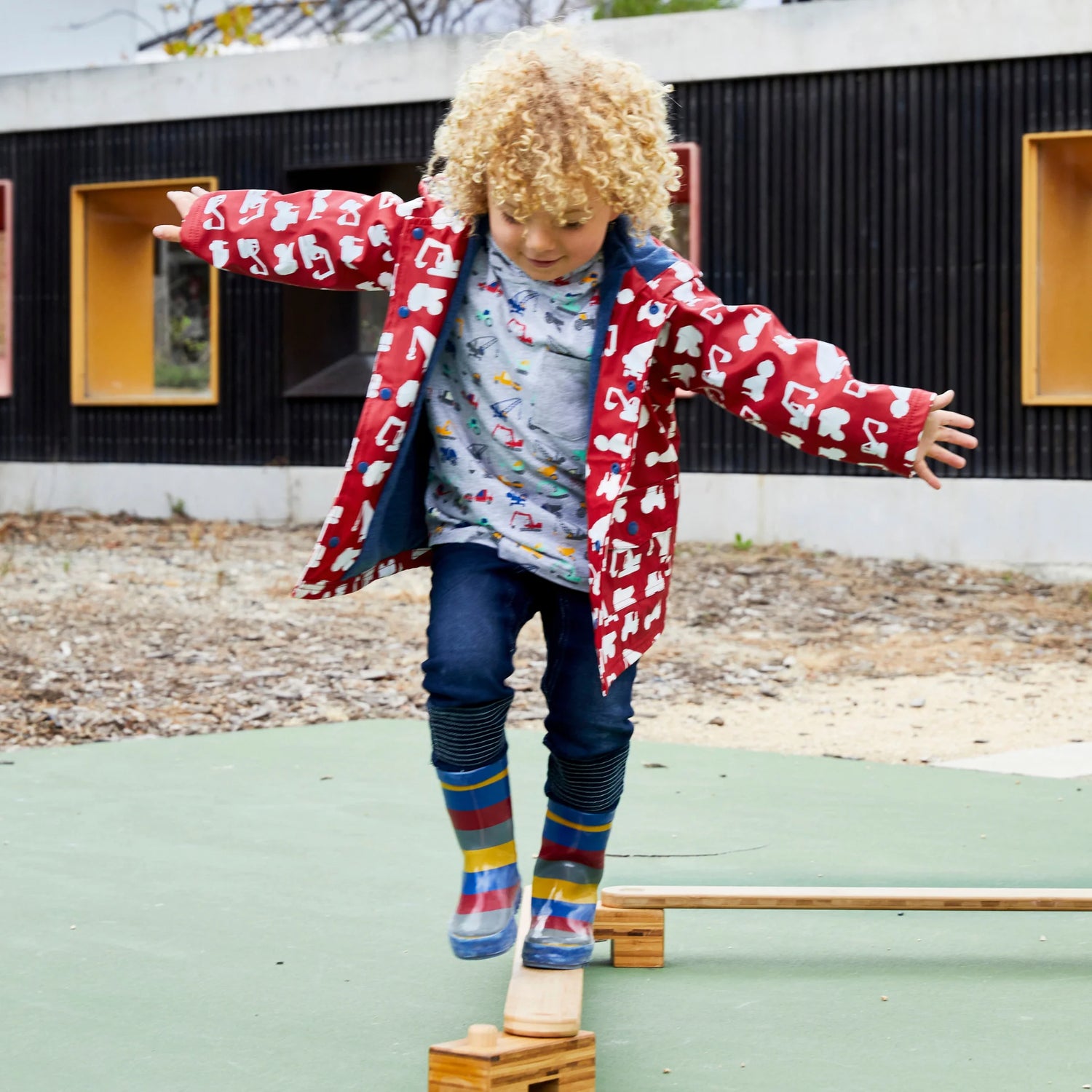 Boy on balancing beam wearing colourful kids gumboots and red raincoat that changes colour