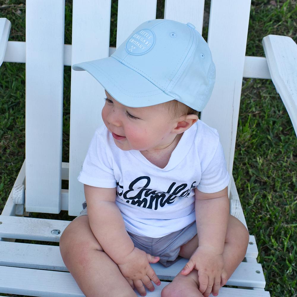 Baby sitting in a chair with a sky Little Renegade Company baseball hat on.