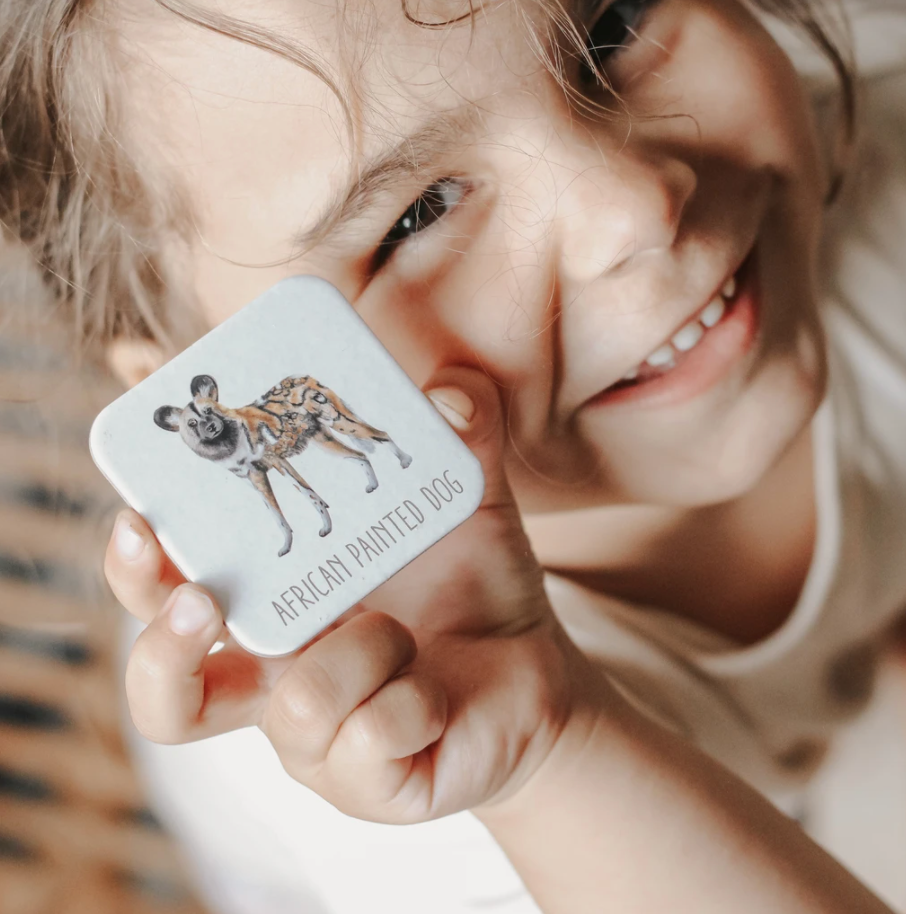 A child smiling and holding a memory game card with an African Painted Dog on it.